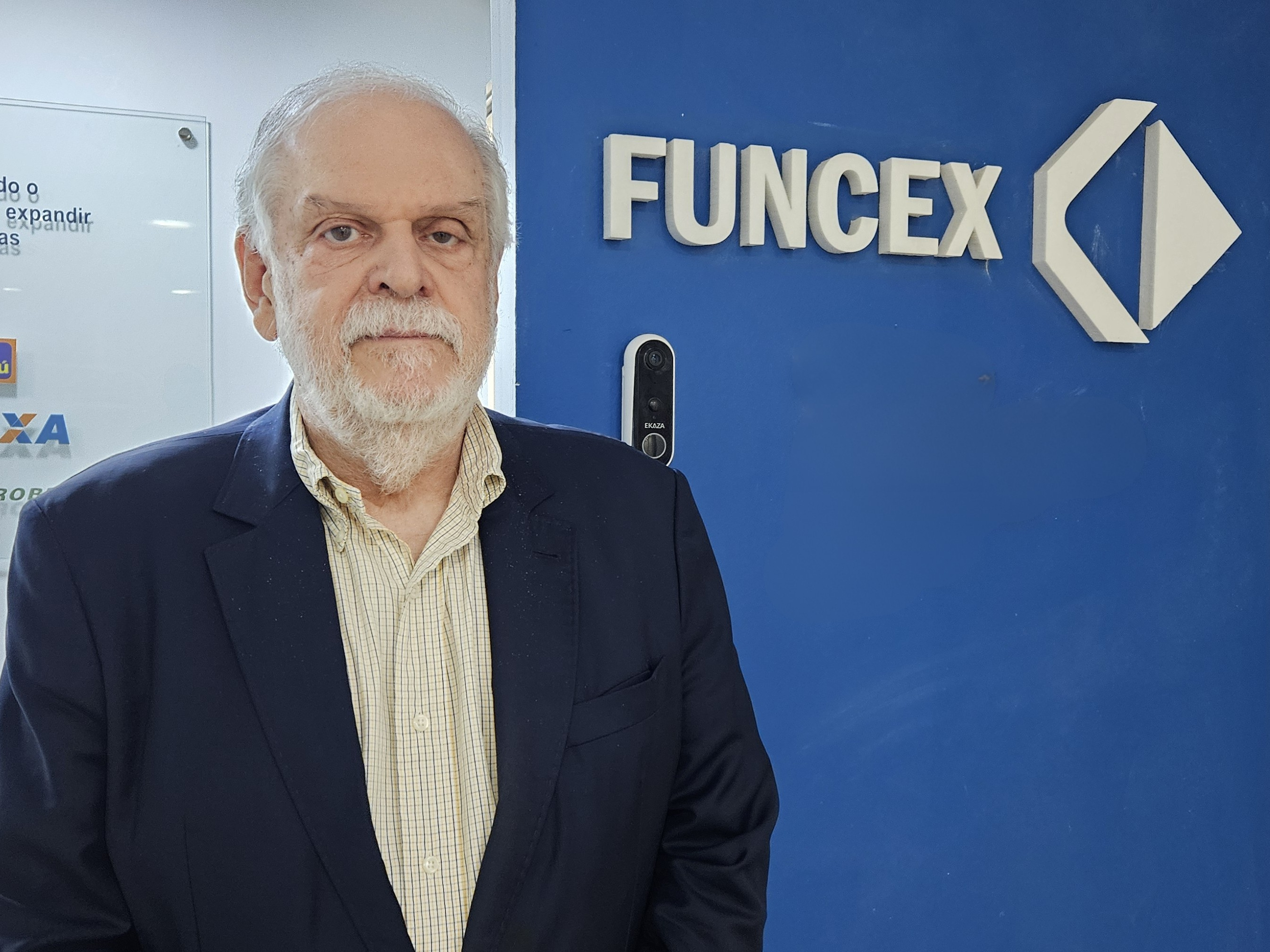 Pessoa de fato em frente a uma parede azul com o logótipo da Funcex, representando o ambiente institucional da fundação mencionada no artigo.