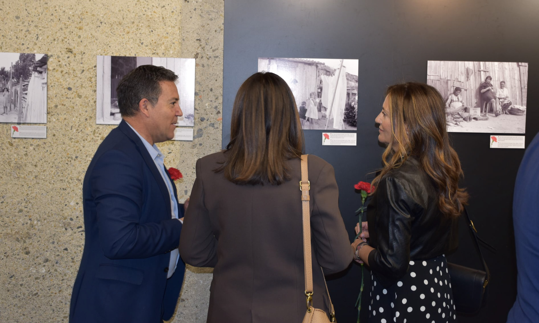 Três pessoas observam fotografias expostas numa parede durante a inauguração da exposição 'Memórias da Ditadura' no centro cultural La Llacuna, em Andorra.