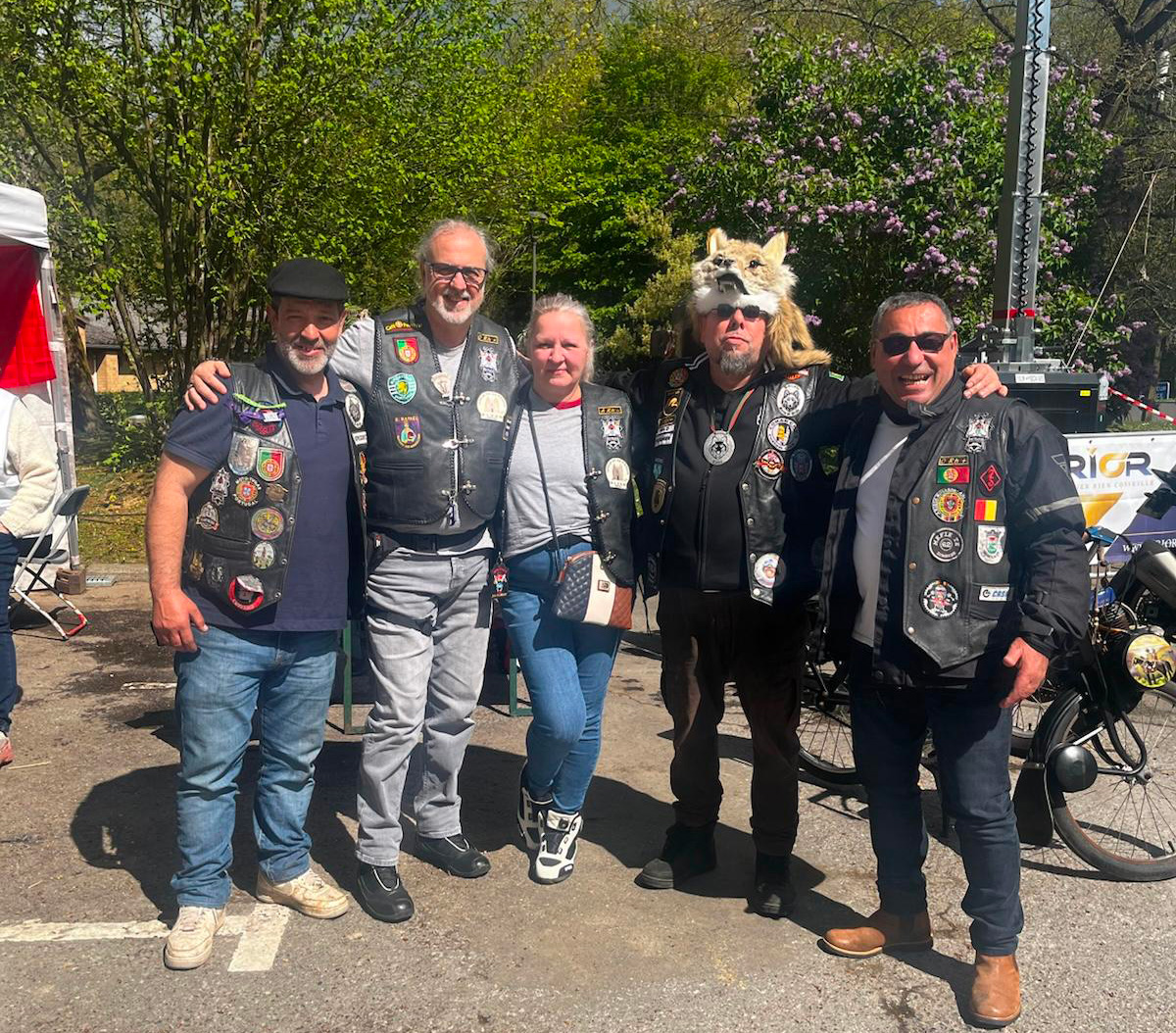 Cinco pessoas com coletes de motard, sorridentes, posam juntas ao ar livre durante o evento solidário dos Lobos Motards ASBL em Rixensart.