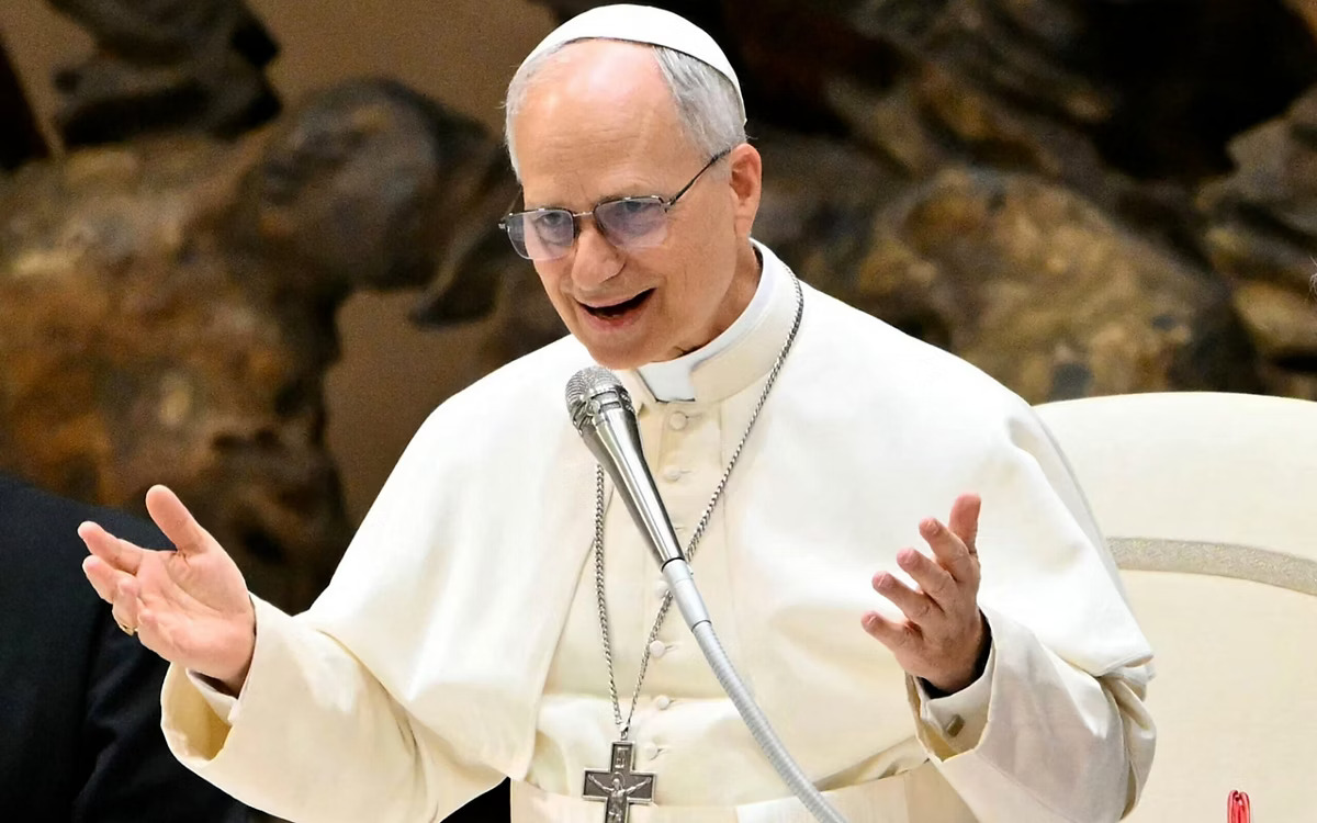 O papa Leão XIV, vestido de branco, discursa num altar decorado com flores amarelas, num ambiente religioso, durante um evento académico em Roma.