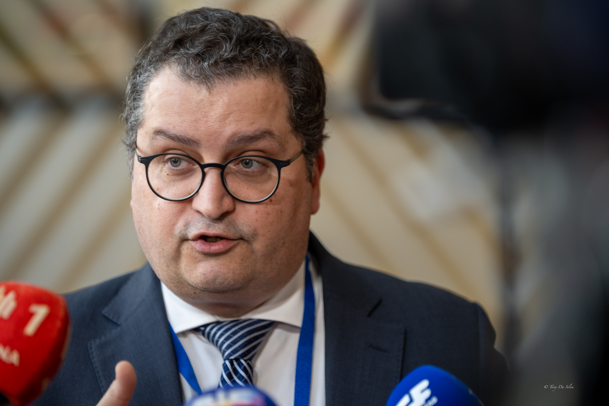 O ministro das Finanças fala à imprensa em Bruxelas sobre o desconto temporário no imposto sobre combustíveis devido à guerra no Médio Oriente, rodeado por microfones de vários órgãos de comunicação social.