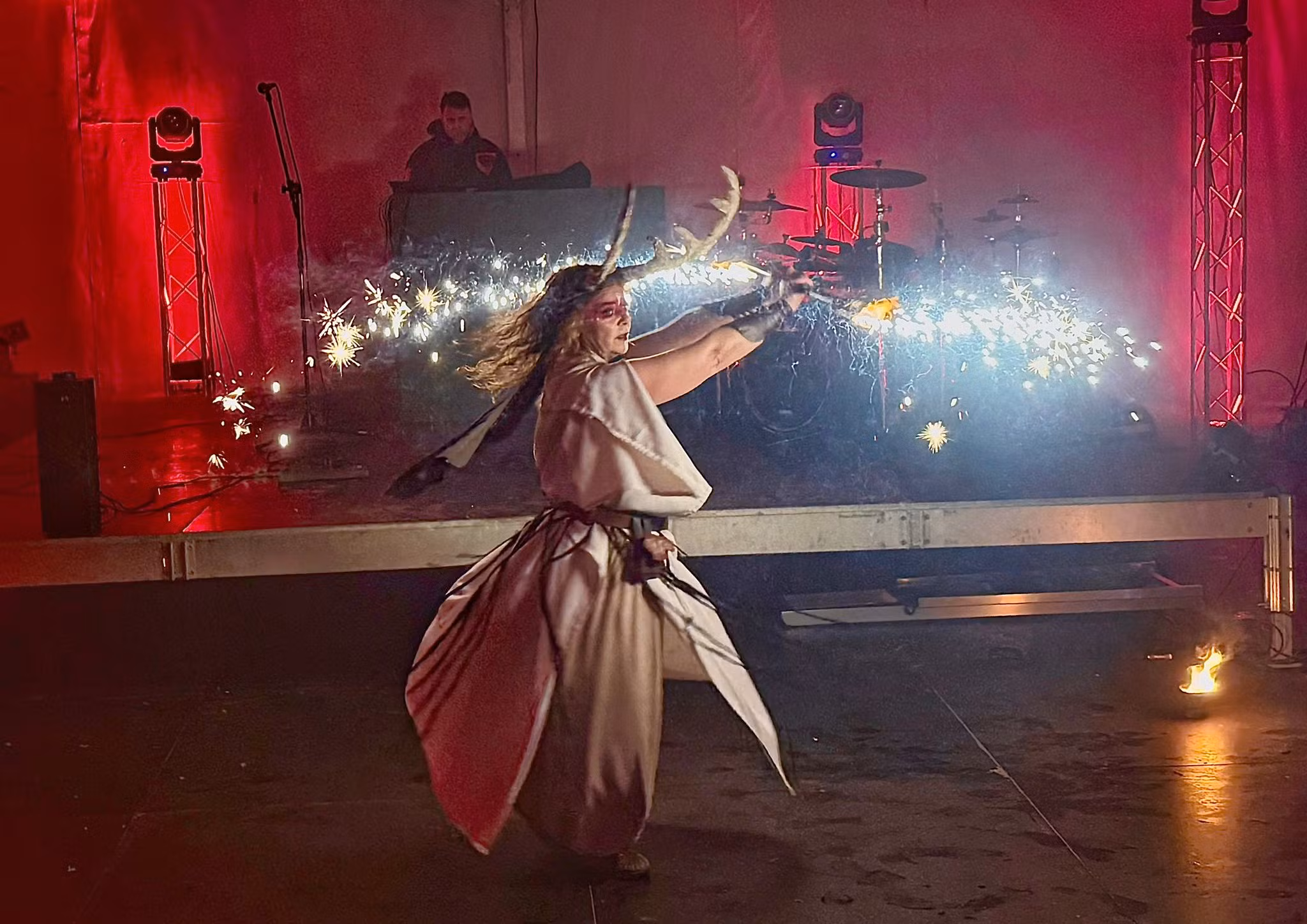 Artista em traje celta executa uma performance com faíscas e luzes diante de um palco iluminado, evocando o ambiente ritualístico e festivo do Magusto Celta de Pitões das Júnias.