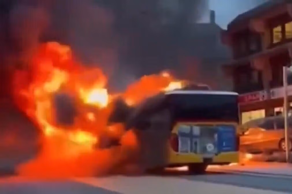 Autocarro de transporte público envolto em chamas intensas numa rua urbana, ilustrando o incêndio descrito no artigo.