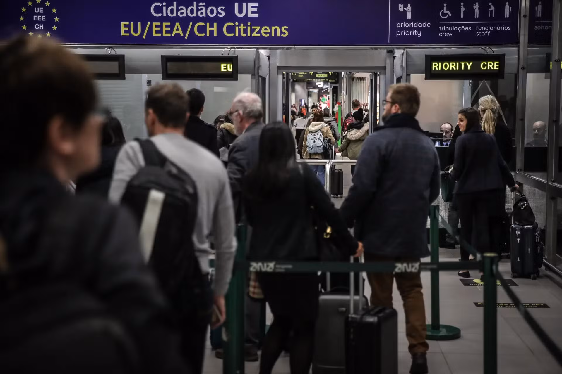 Passageiros em fila numa zona de controlo de fronteiras de aeroporto, junto a uma placa para cidadãos da UE/EEE/Suíça, ilustrando tempos de espera e controlo reforçado referidos no artigo.